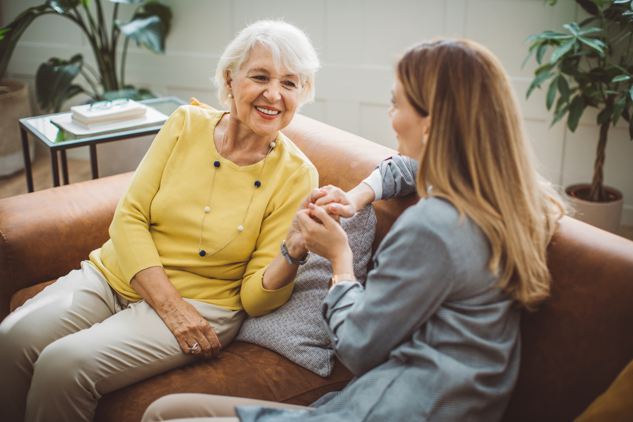 A senior woman and her daughter are sitting on a couch having a conversation.