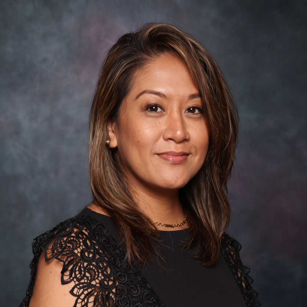 Portrait of a woman with shoulder-length hair in a black lace dress, standing against a dark textured backdrop.