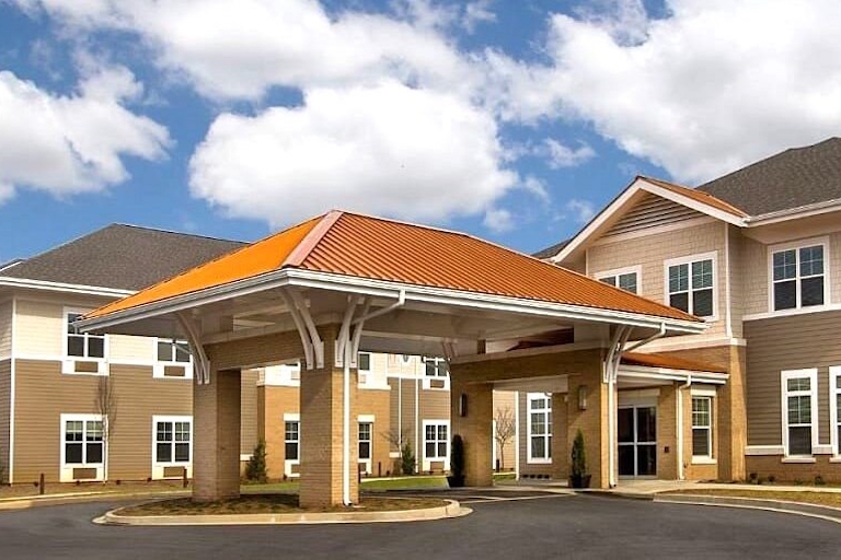 Brick building with an orange-roofed porte-cochère over the entrance on a sunny day.